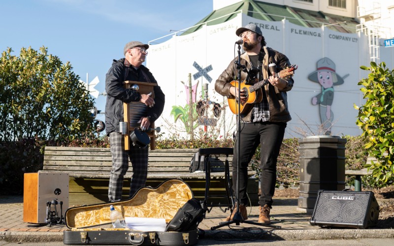 Two men signing at Freeze Ya Bits Off Busking in Gore with SGT Dan in the background 