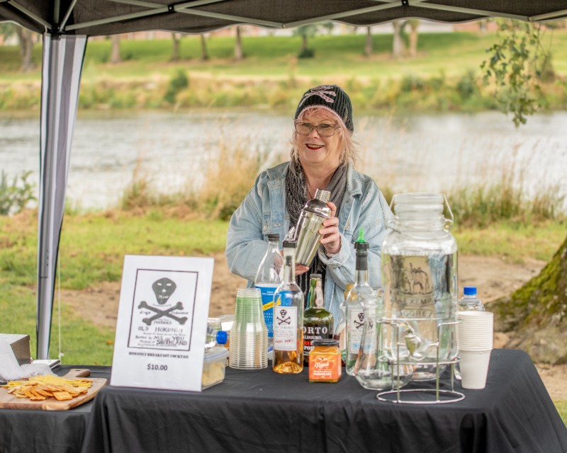 Lady holding cocktail shaker at the Hokonui Moonshine Cocktail stall at On the Fly River Festival in Gore Southland. 