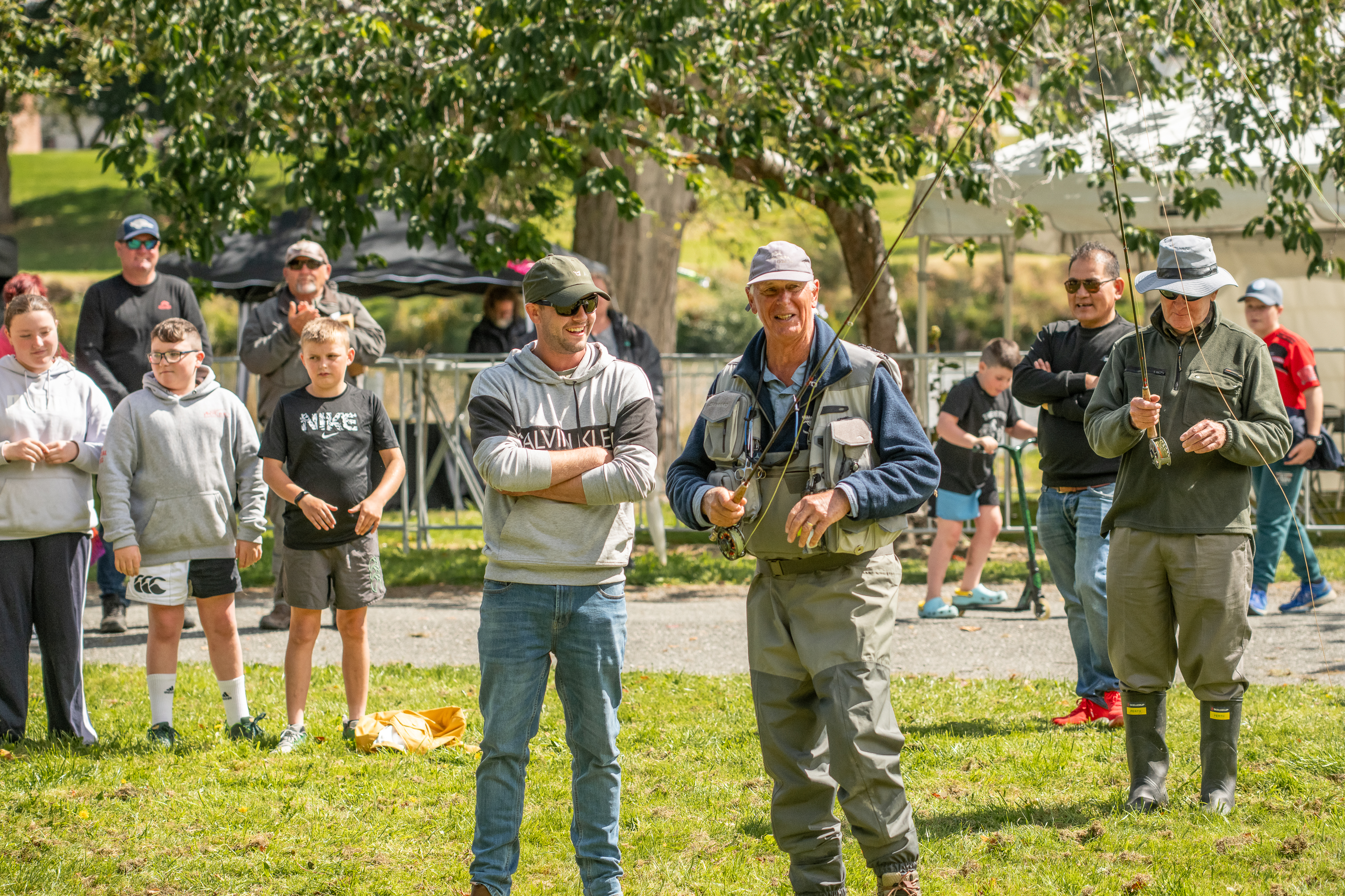 Fishing Guide teaching a man to cast at On the Fly event by the Mataura River. There are people behind watching the man getting taught to cast. 