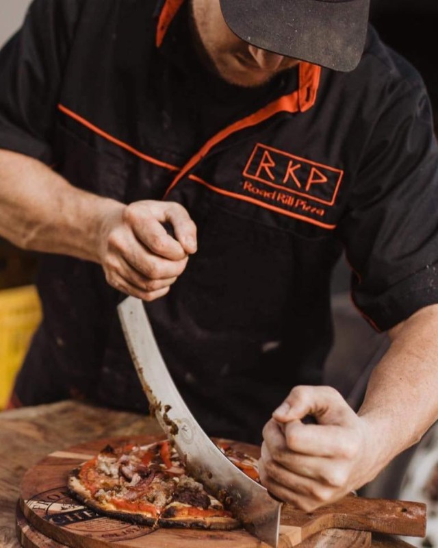 Man from Road Kill Pizza cutting up a freshly baked pizza at On the Fly River Festival in Gore Southland 